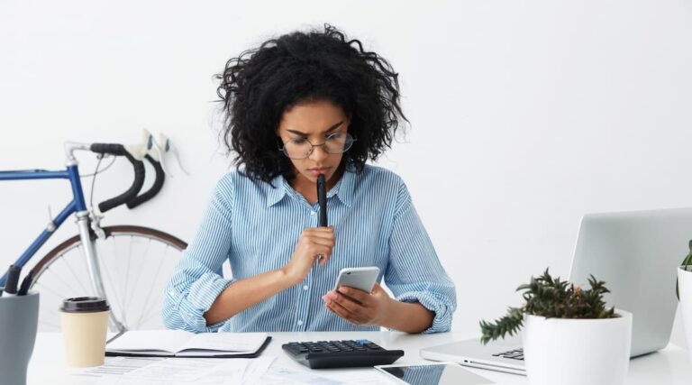Uma mulher lojista sentada em sua mesa de trabalho e aprendendo a como calcular o frete dos seus produtos||calcular frete imagem caixa com etique