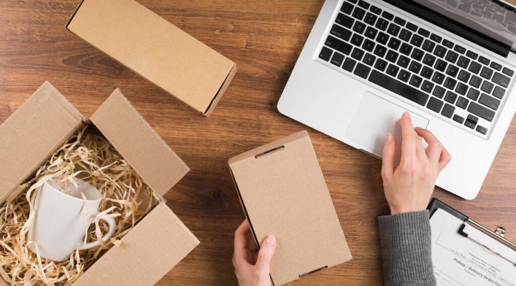 Lojista fazendo picking, ele está separando e embalando suas vendas com caixas de papelão ao lado de um notebook||o que é picking