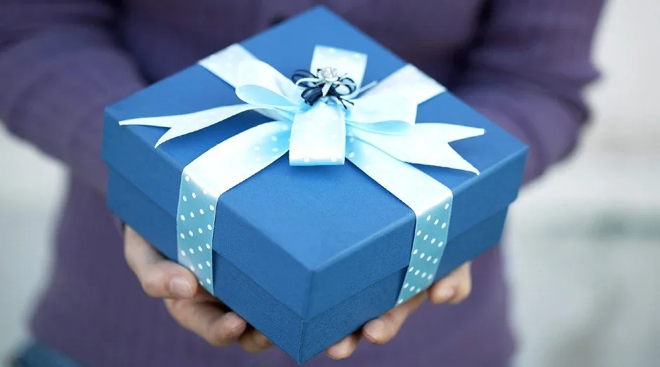 Embrulho de presente azul sendo entregue por mãos femininas||